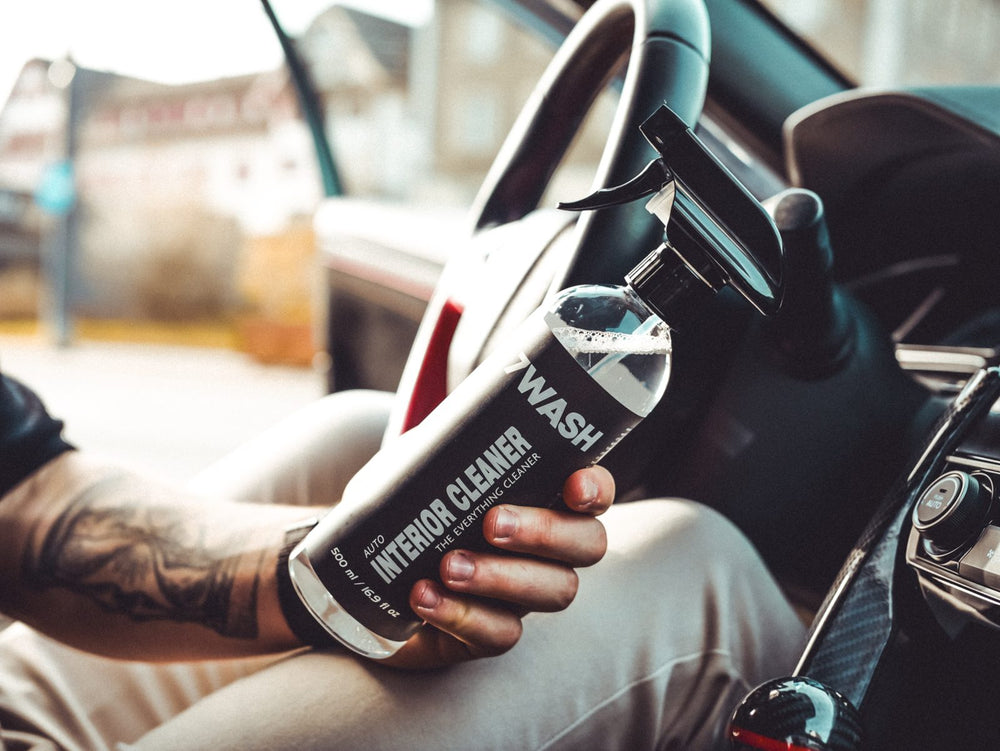 Hand holding a bottle of 7WASH Interior Cleaner next to the steering wheel of a car