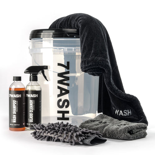 7WASH Starter Wash kit featuring a transparent wash bucket with black branding, one 500ml bottle of premium auto wash shampoo, a grey microfiber wash mitt, a grey drying towel, and a large black microfiber cloth.