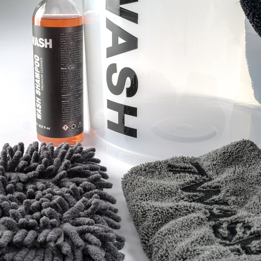 7WASH Starter Wash kit featuring a transparent wash bucket with black branding, one 500ml bottle of premium auto wash shampoo, a grey microfiber wash mitt, a grey drying towel, and a large black microfiber cloth.