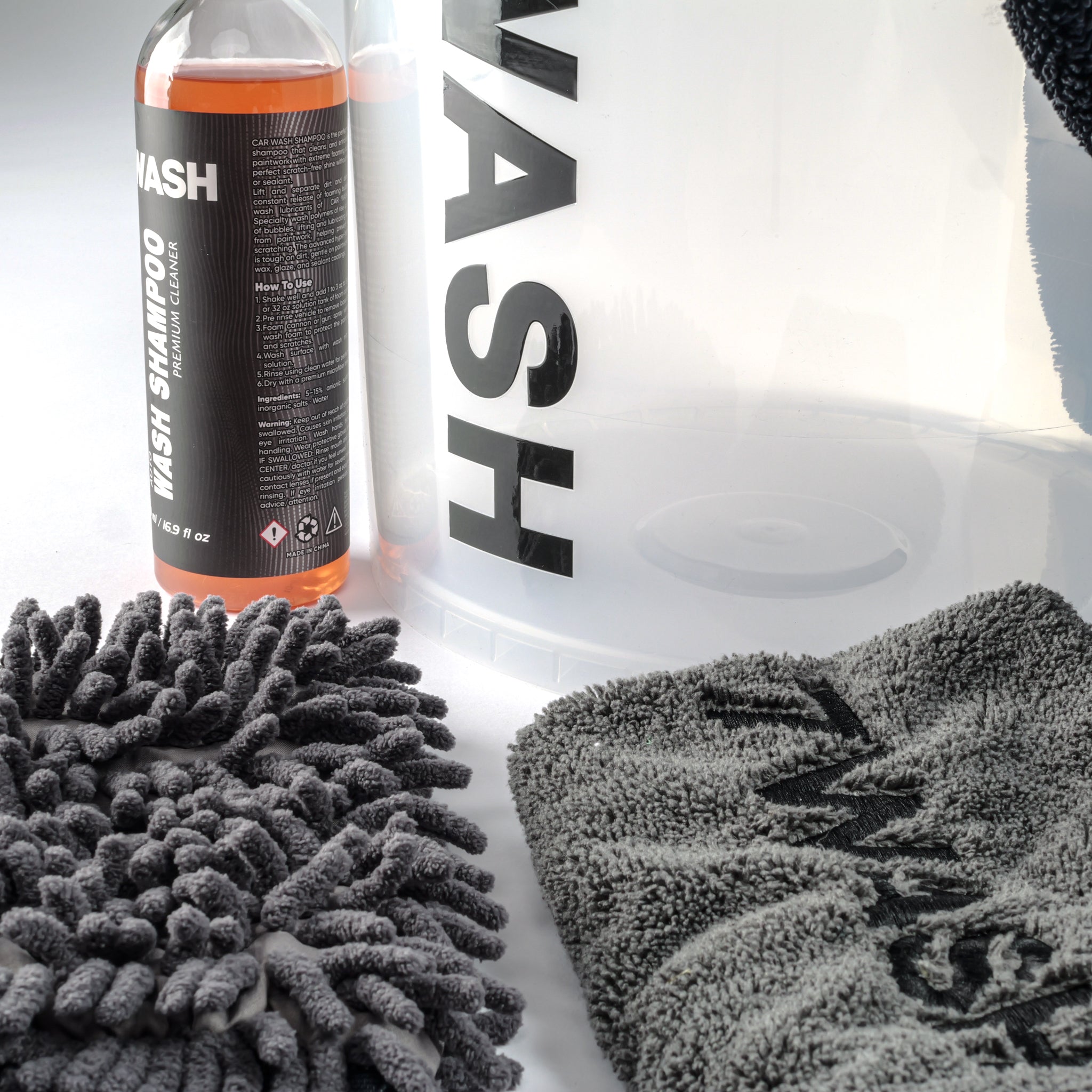 7WASH Starter Wash kit featuring a transparent wash bucket with black branding, one 500ml bottle of premium auto wash shampoo, a grey microfiber wash mitt, a grey drying towel, and a large black microfiber cloth.