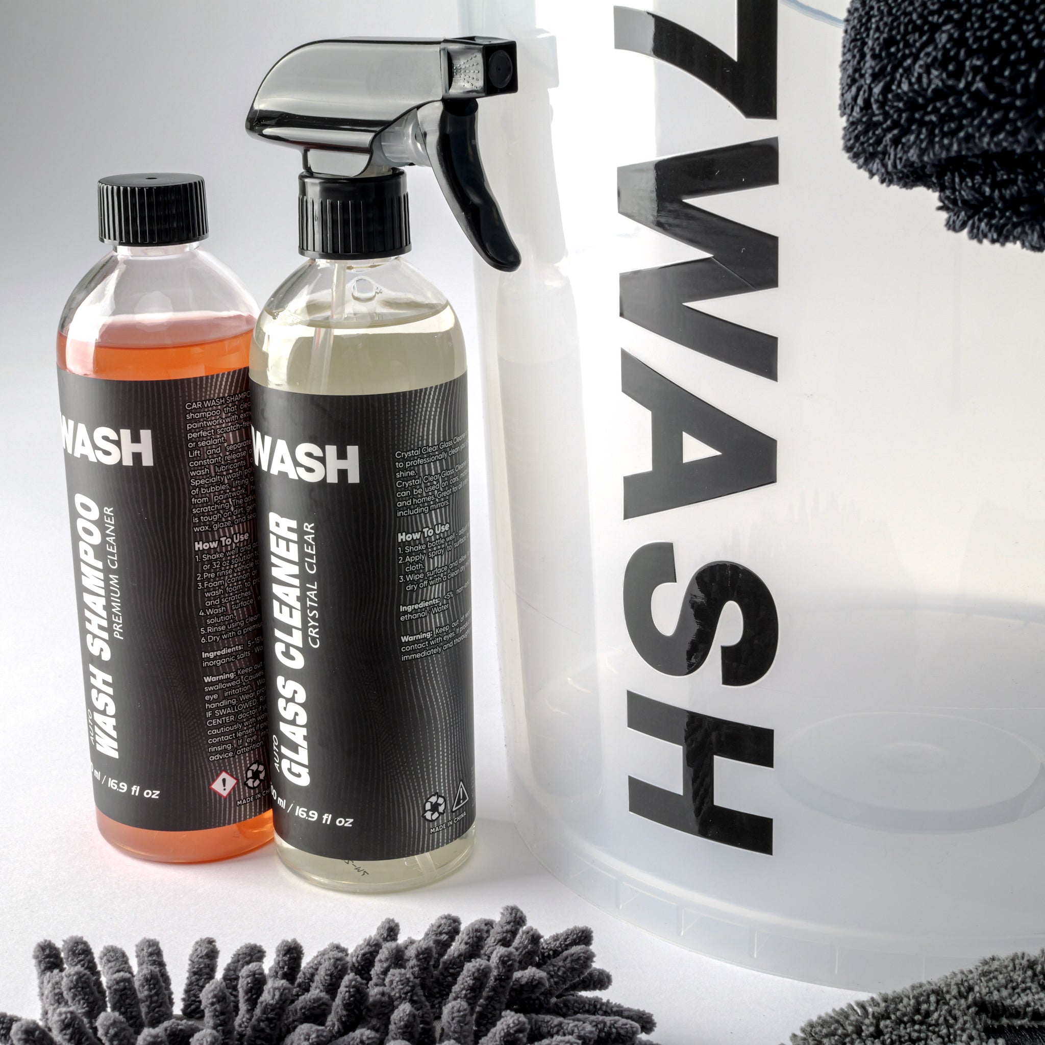 7WASH Starter Wash kit featuring a transparent wash bucket with black branding, one 500ml bottle of premium auto wash shampoo, a grey microfiber wash mitt, a grey drying towel, and a large black microfiber cloth.